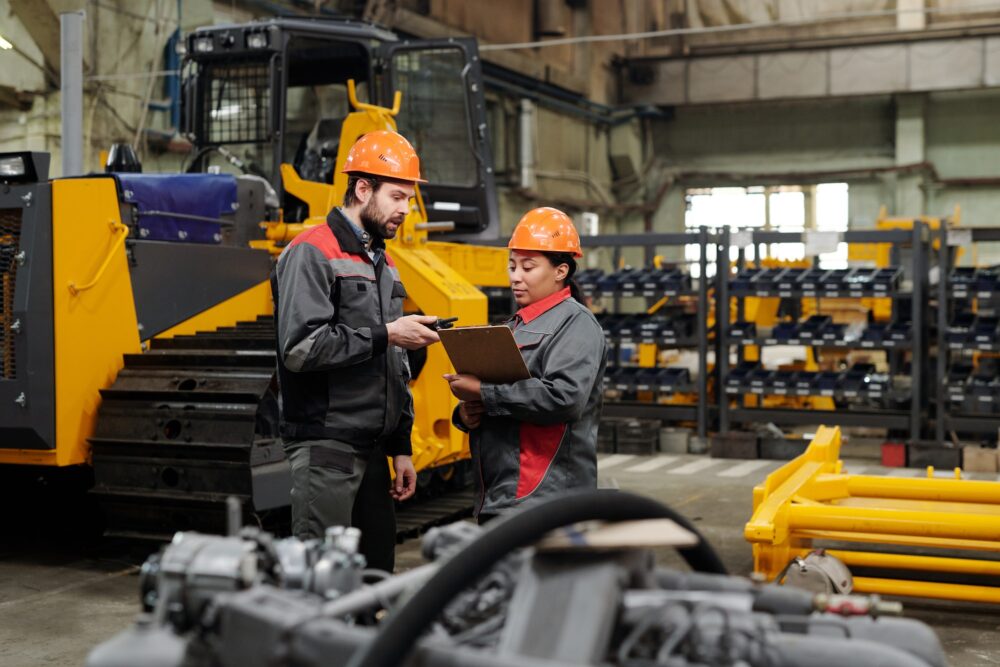 Two young workers of industrial plant in workwear discussing data in document